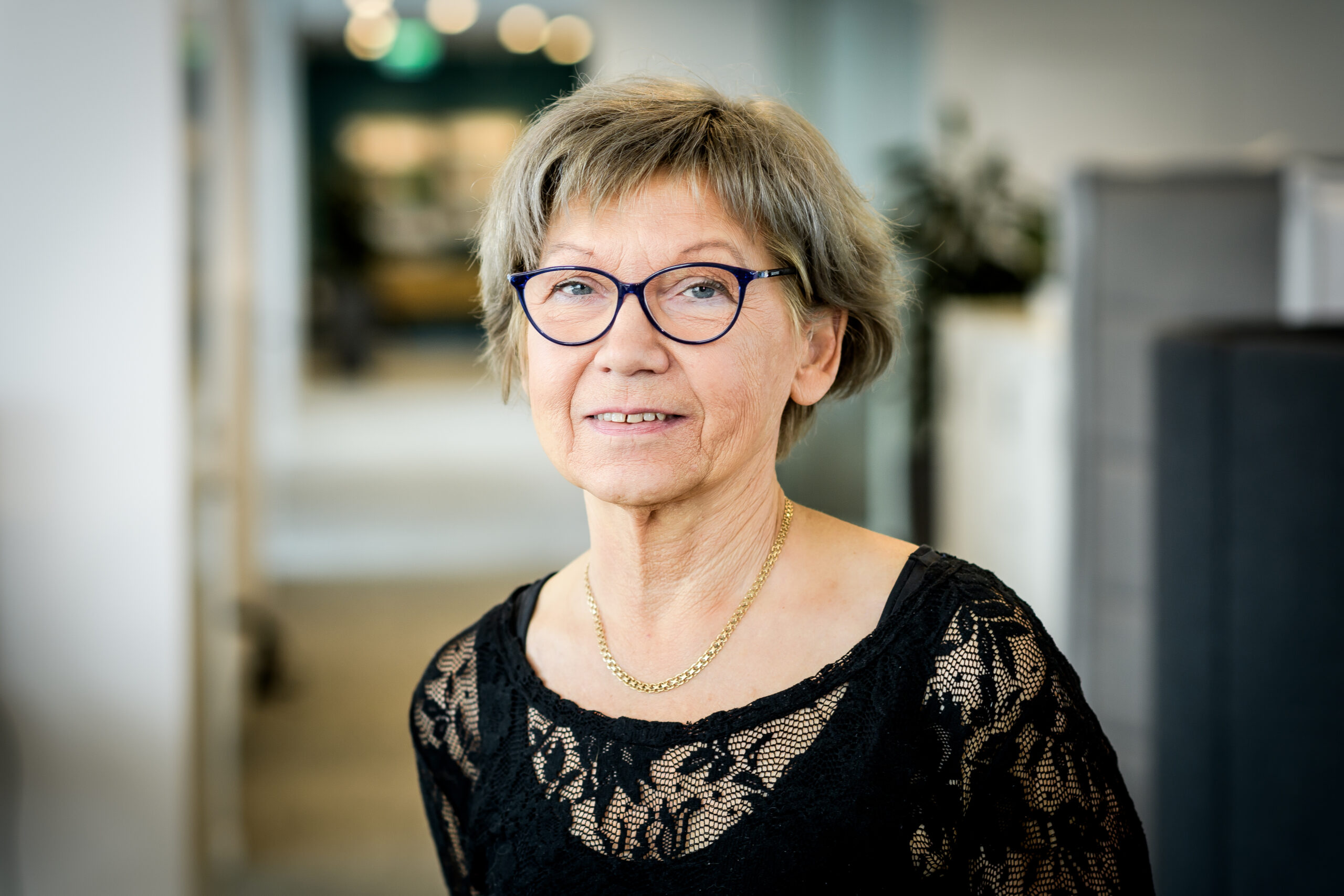 Porträttbild på Lena Levin mot en suddig bakgrund i kontorsmiljö.