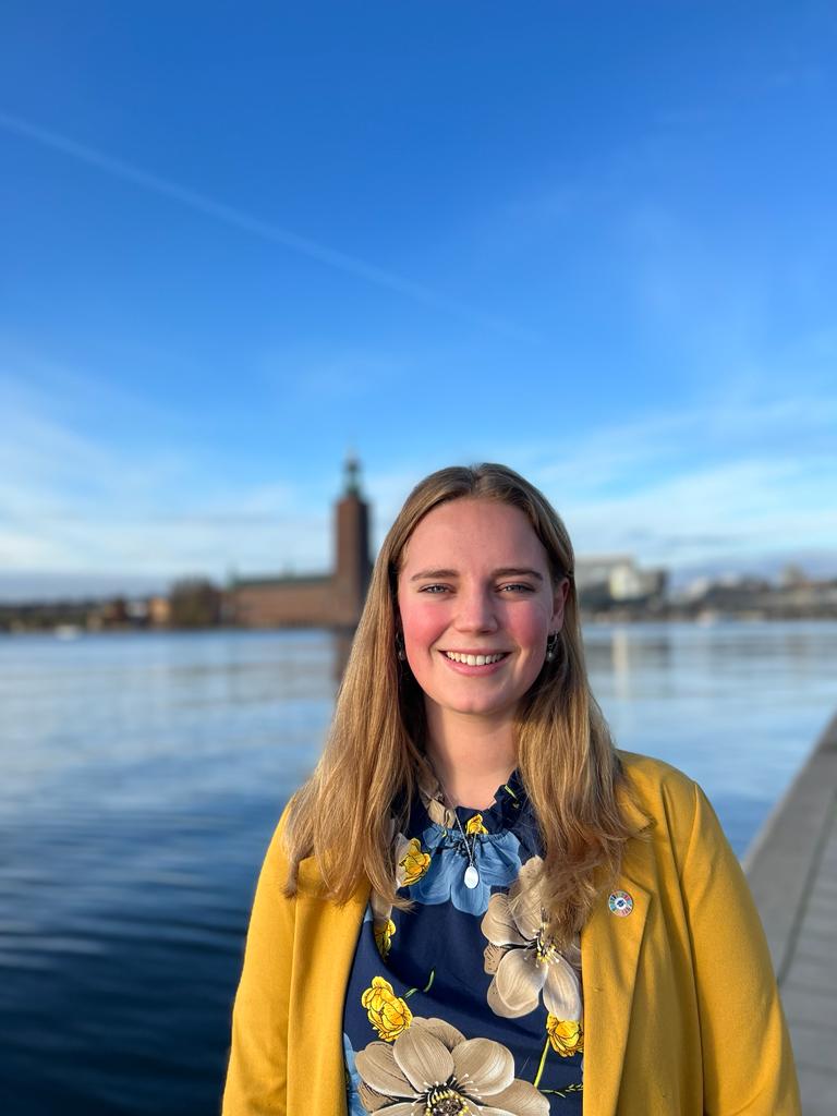 Michelle van Ardenne står framför vattnet med Stockholms stadshus i bakgrunden en solig dag.