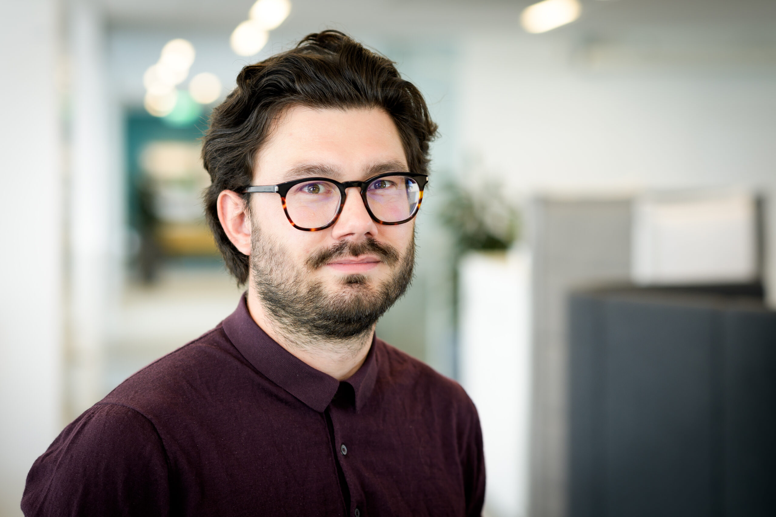 Porträttbild på Jakob Allansson mot en suddig bakgrund som visar en kontorsmiljö.