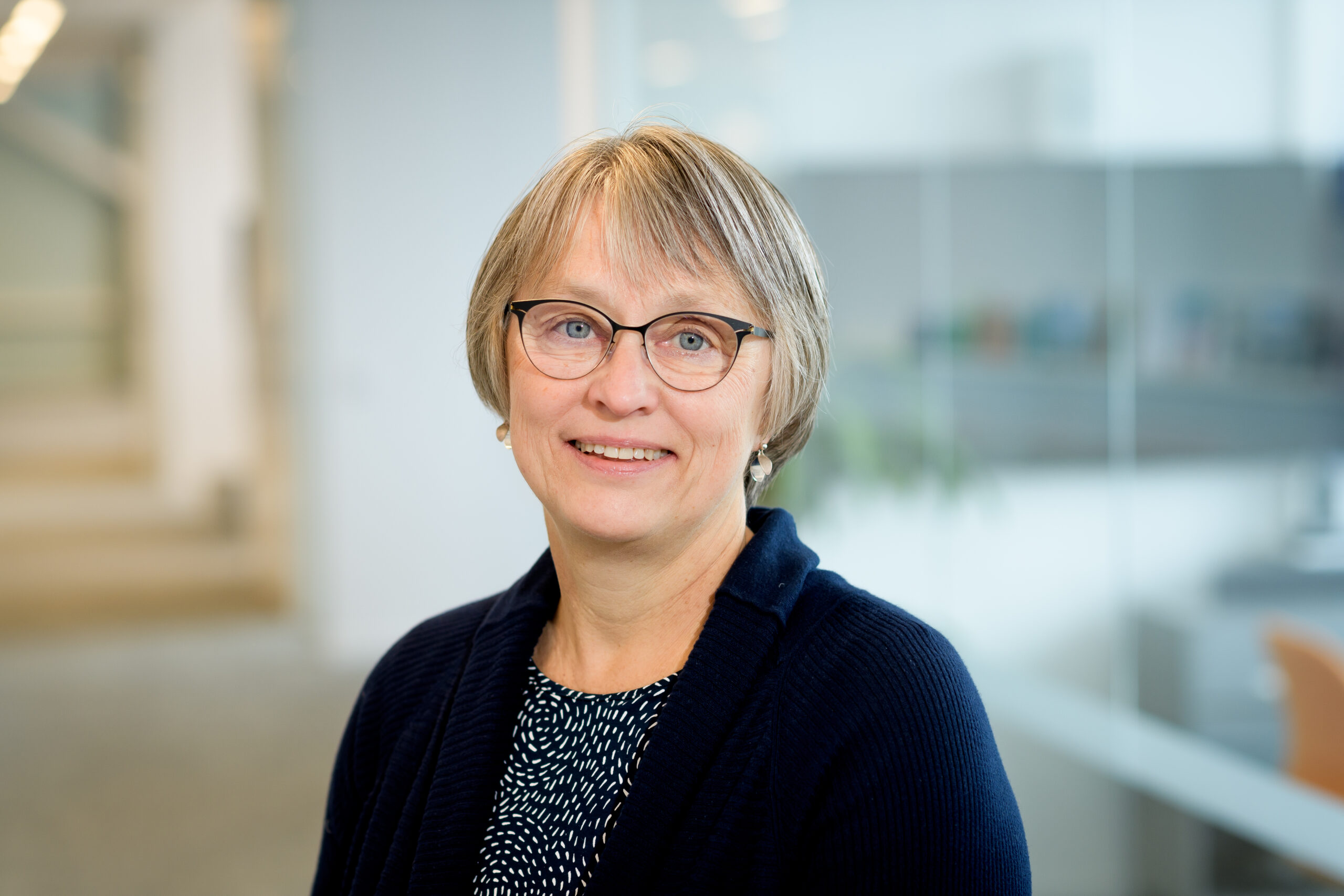 Porträttbild på Gunilla Carlsson mot en suddig bakgrund som visar en kontorsmiljö.