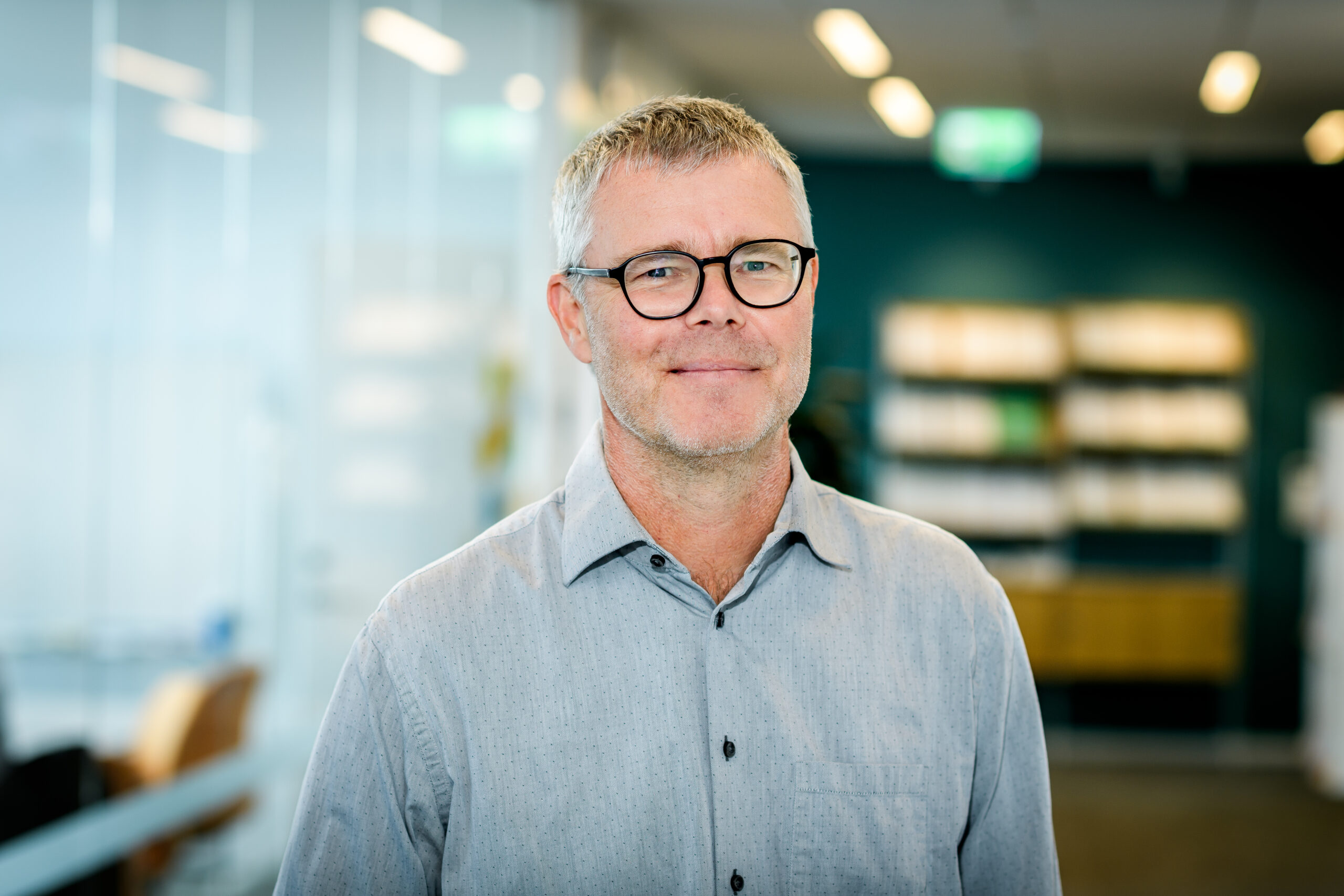 Porträttbild på Jan Persson mot en suddig bakgrund som visar en kontorsmiljö.