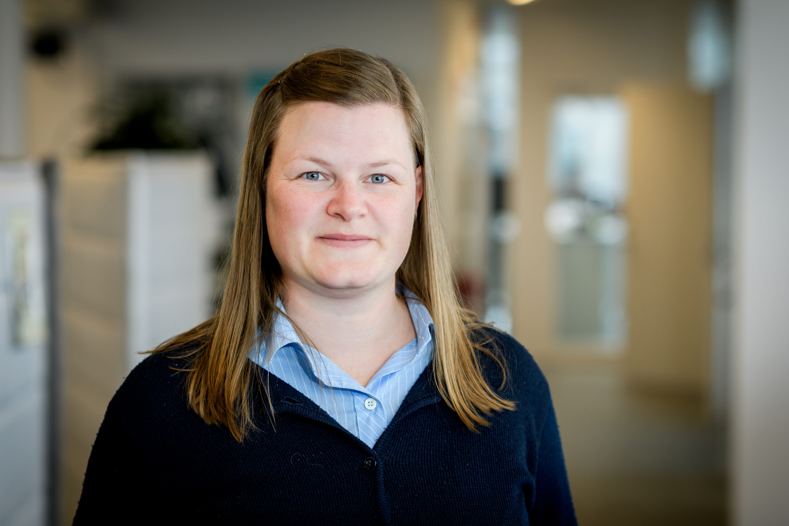 Porträttfotografi på Eva-Lena Eriksson mot en suddig bakgrund som visar en kontorsmiljö.