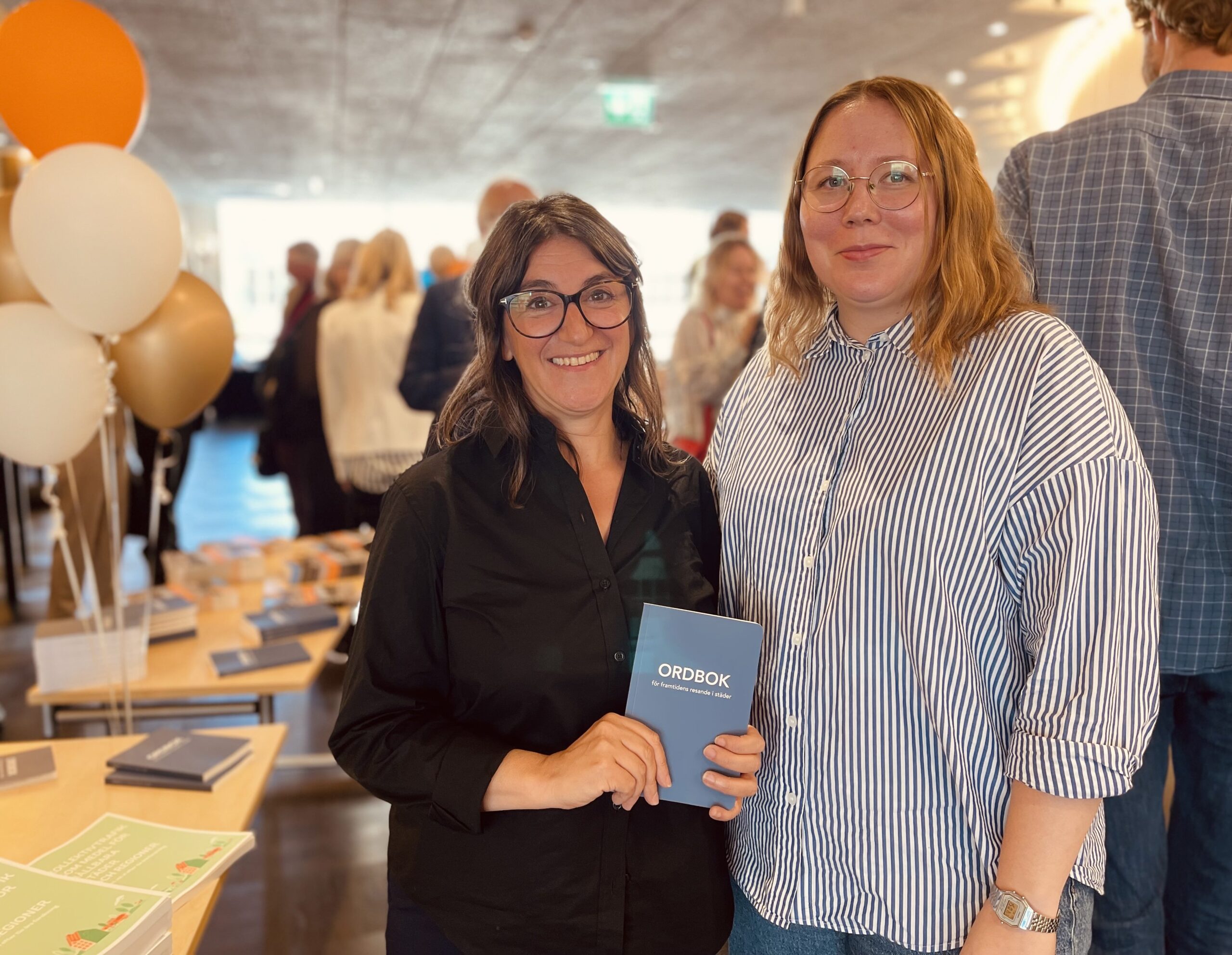 Dalia Mukhtar-Landgren och Sara Ringvall Sundkvist ler mot kameran och håller i en bok.