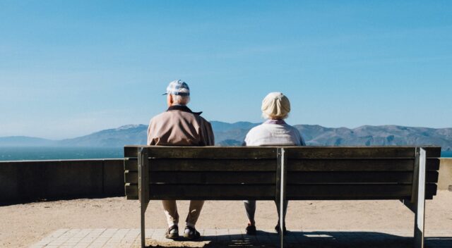 Elderly couple sitting on a bench, seen from behind. Photo.