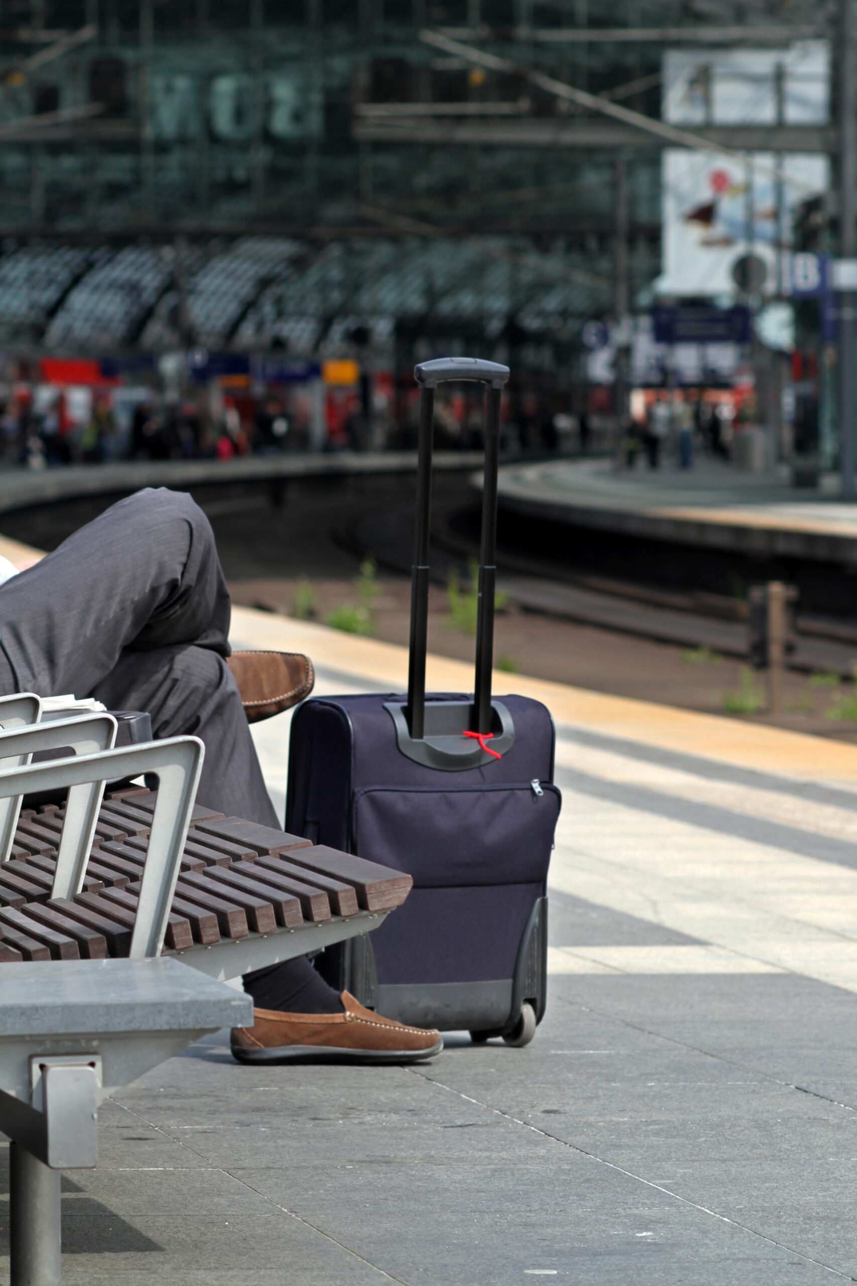 Resenär väntar med väska på en station. Foto.