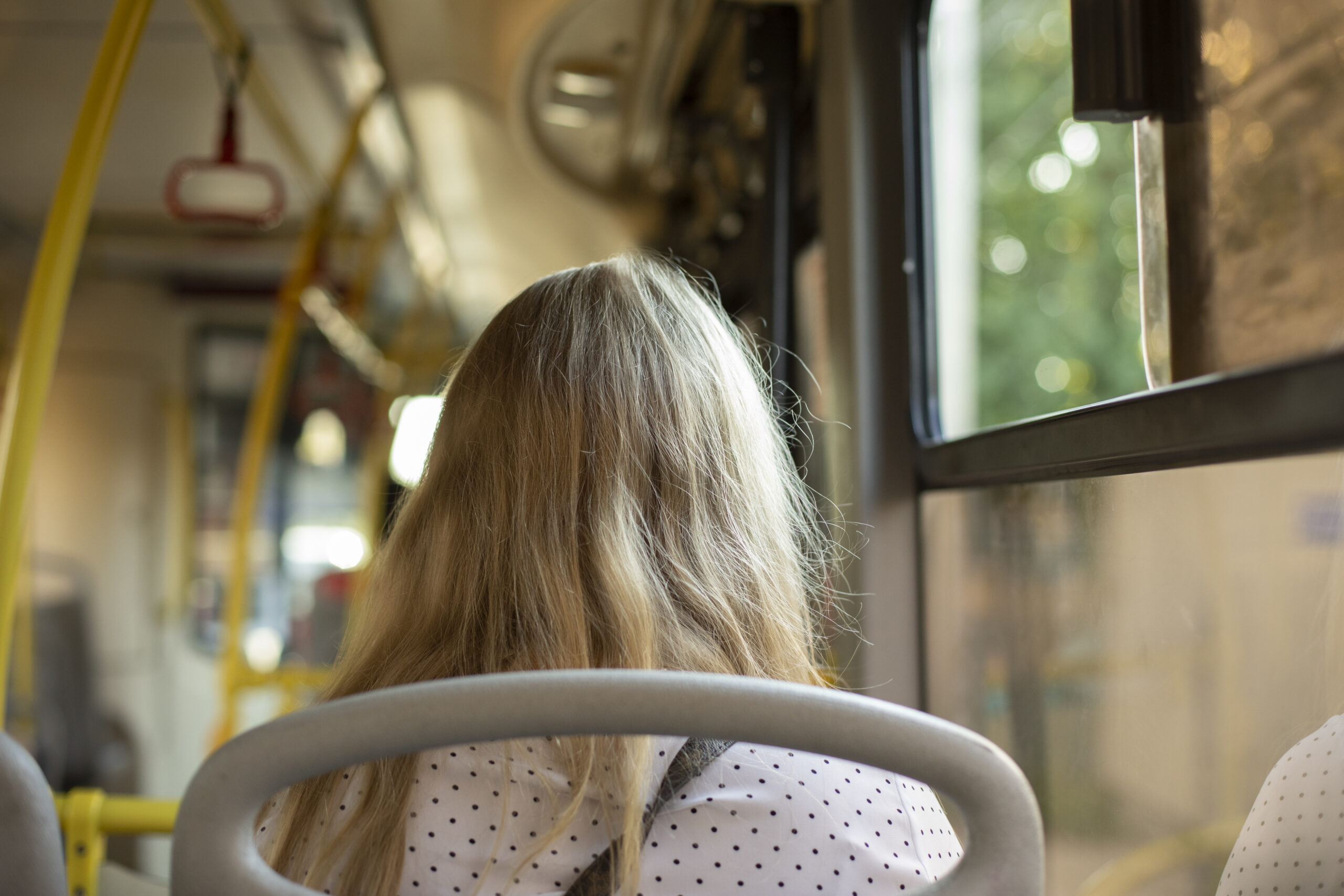 En flicka sitter på en buss, fotograferad bakifrån, med baksidan av hennes huvud synlig.