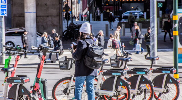 Kvinna på väg att hyra cykel eller elspark. Foto.