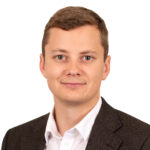 En man med kort brunt hår, mörk kavaj och vit skjorta. Foto.